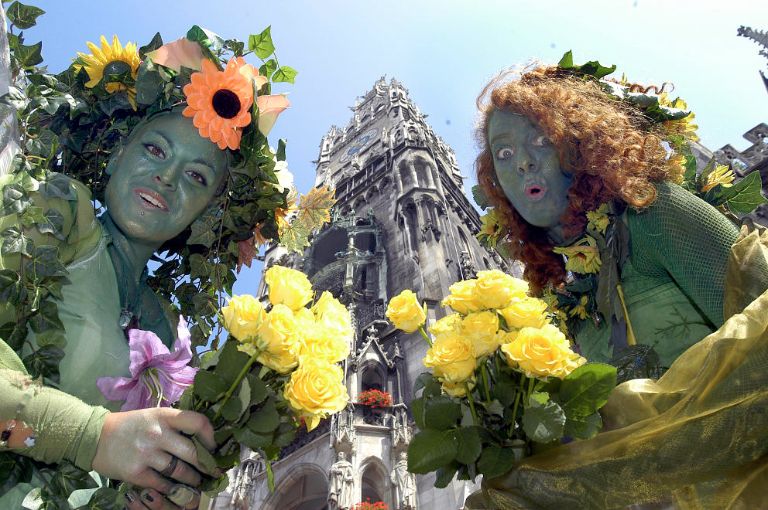 Stelzengängerinnen grüßen mit Blumensträußen