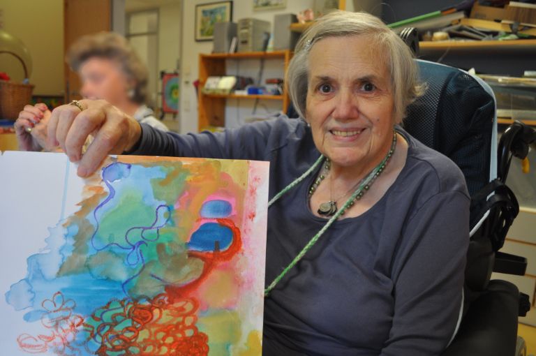 Eine ältere Frau zeigt ihr selbstgemaltes Bild.