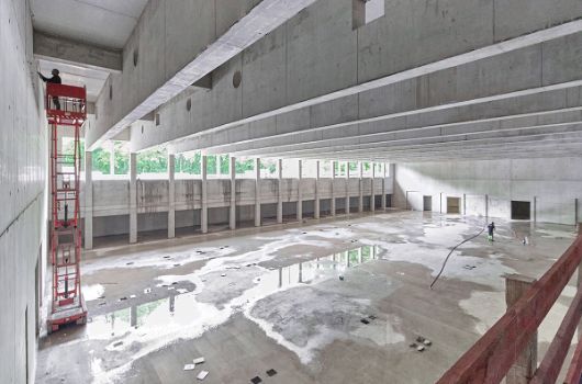 Blick von der Tribüne in die bereits ausgeschalte Sporthalle; weitgespannte Unterzüge verteilen die Lasten aus den darüberliegenden, in Holzbauweise erstellten Lernhäusern