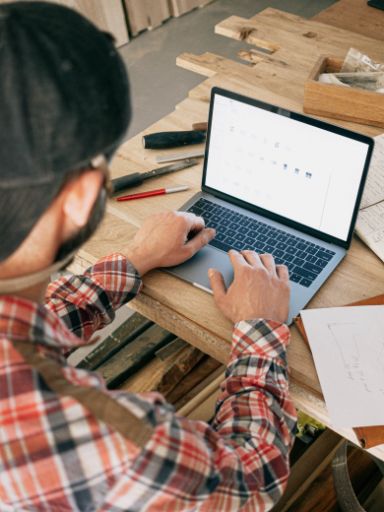 Junger Mann sitzt vor einem Laptop. Neben dem Laptop liegen technische Zeichnungen.